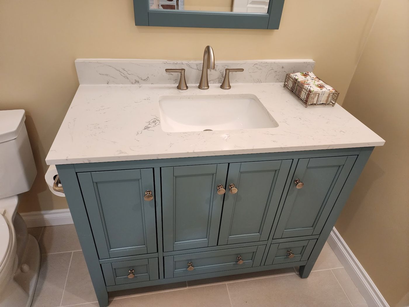 A painted slate-blue shaker vanity with a marbled quartz top, undermount basin, brushed nickel tap and a matching framed mirror.